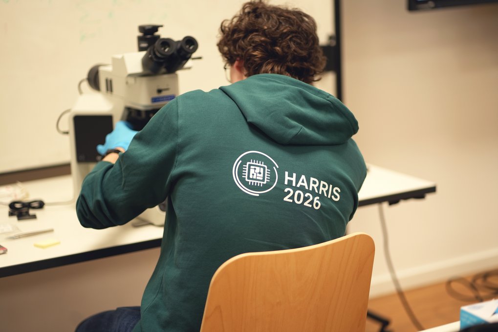 Eine Person in einem Kapuzenpulli mit dem Logo der Veranstaltung schaut durch ein Mikroskop