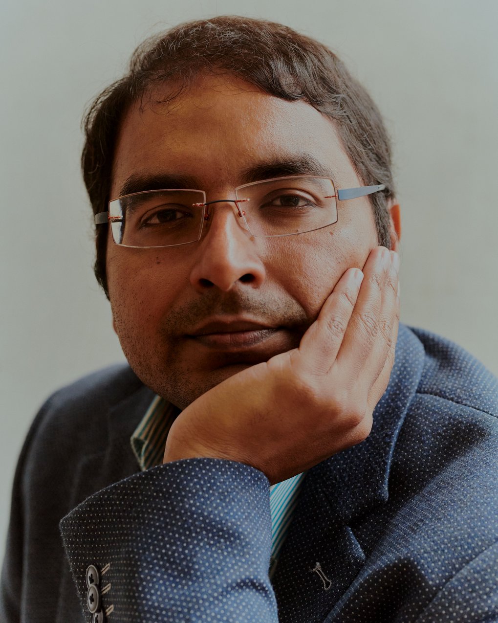 Porträt von Krishna Gummadi mit randloser eckiger Brille und blauem Jacket, das Kinn auf die Hand gestützt.