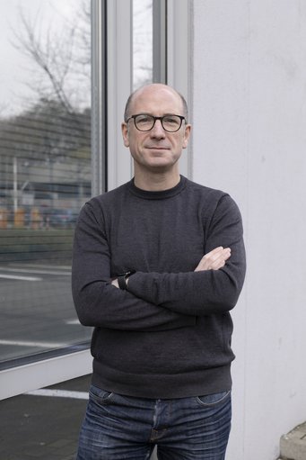 Thorsten Holz, Direktor am Max-Planck-Institut für Sicherheit und Privatsphäre. Ein Mann mit Brille und dunklem Pullover steht mit verschränkten Armen vor einem Fenster, in dem sich Bäume und ein Parkplatz spiegeln.