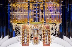 Im inneren des Quantencomputers von IBM ist der turmförmige Kryostat zu sehen, in dem zahlreiche silbrige Leitungen und Streben zwischen zwei goldenen Scheiben verlaufen.Die Leitungen enden unter der unteren Scheibe mit goldenen Steckern in Steckerleisten.