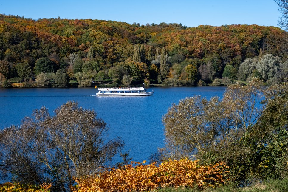 A white boat on a blue lake surrounded by trees in autumnal colours.